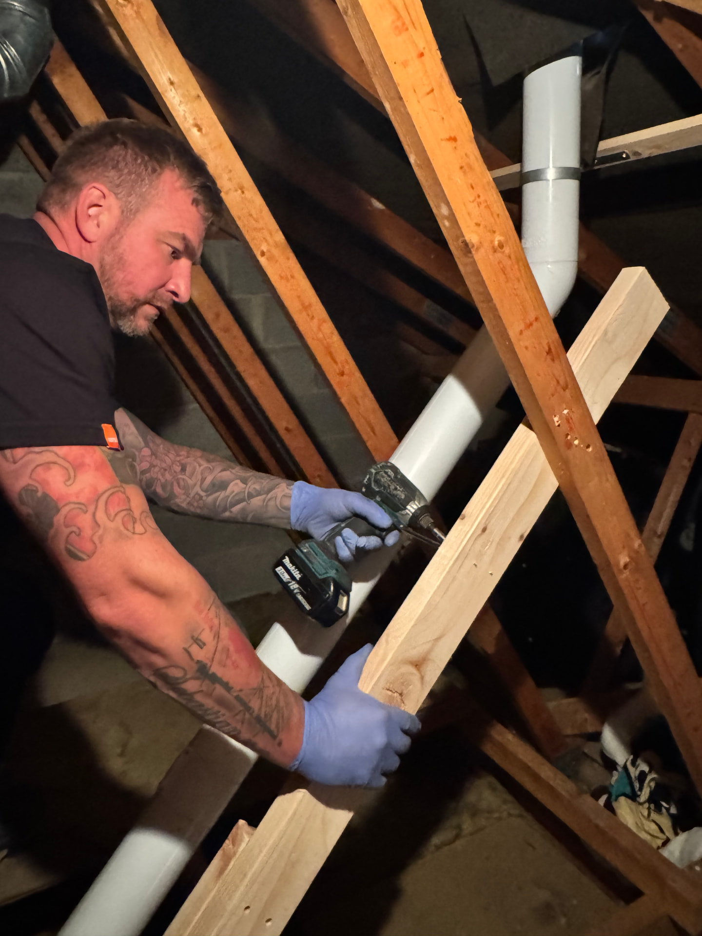 Engineer installing pipework and fixings in a loft space with wooden beams